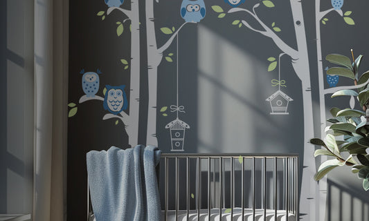 Modern nursery with large birch tree and blue owl wall decals on a dark grey wall above a minimalist crib. Blue owls perch on branches with hanging birdhouses, creating a cozy, nature-themed space.